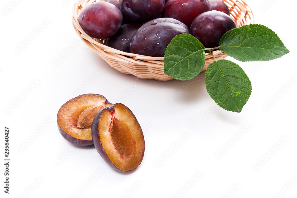 Yellow wooden basket with ripe plums, whole and half ripe plums isolated on a white background.. Yellow wooden basket with ripe plums, whole and half ripe plums isolated on a white background..