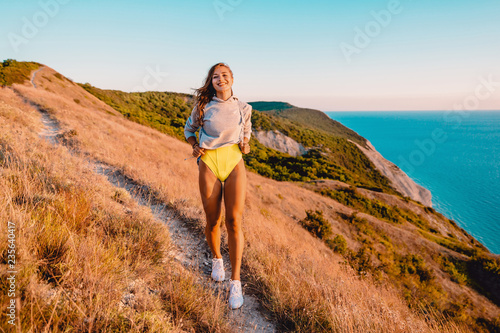 Attractive smiled woman walk in outdoor at warm sunset. Happy holiday in the mountains
