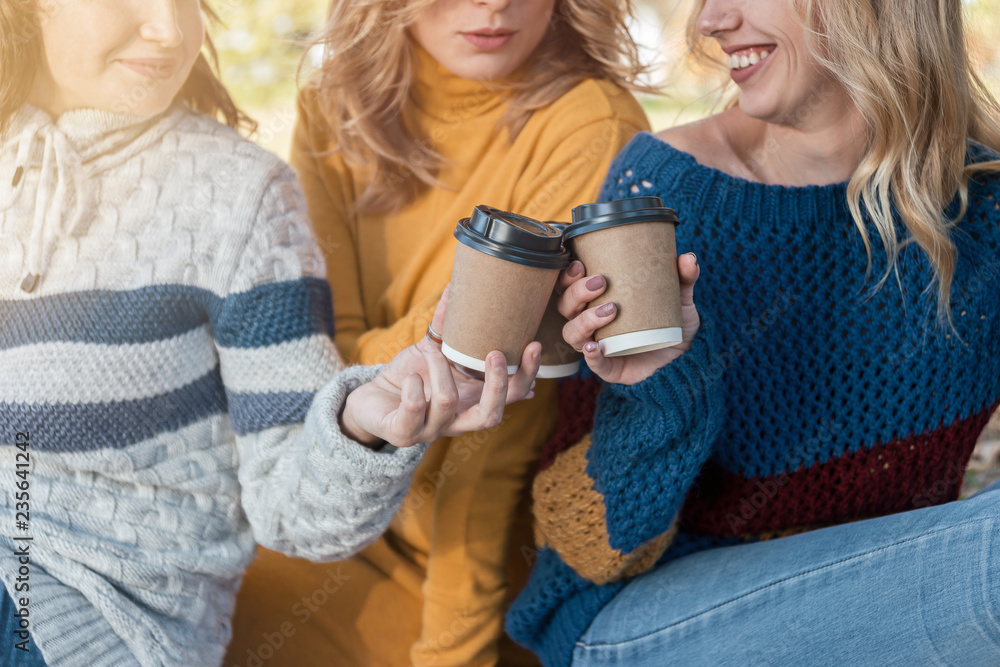 Paper cups of coffee in hands of smiling attractive women.