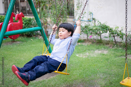 A boy is playing a swing with his brother at the playground.