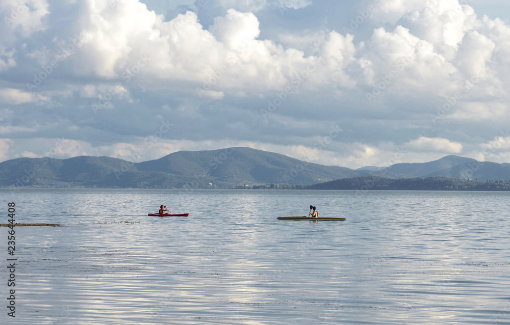 Umbria, Italy, a stretch of Trasimeno lake with canoeists in explorationand and mountains in the background Umbria, Italy, a stretch of Trasimeno lake with canoeists in explorationand and mountains in the background