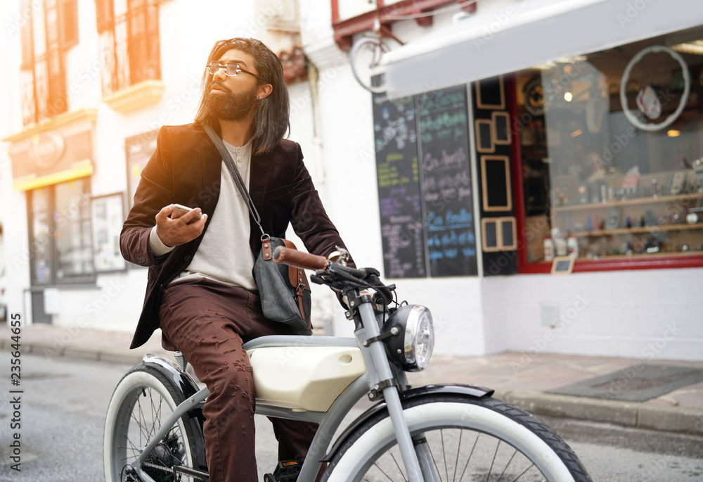Obraz premium Hipster guy with electric vintage style bike using smartphone