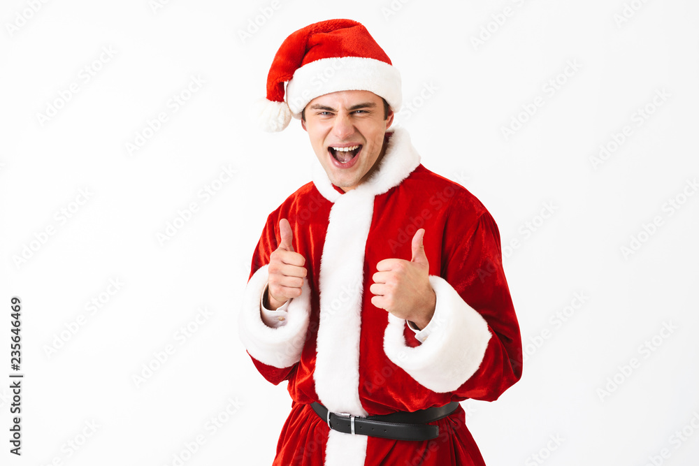 Portrait of positive man 30s in santa claus costume and red hat laughing with thumbs up, isolated over white background in studio Portrait of positive man 30s in santa claus costume and red hat laughing with thumbs up, isolated over white background in studio
