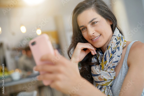 Cheerful woman in coffee shop using smartphone for video call