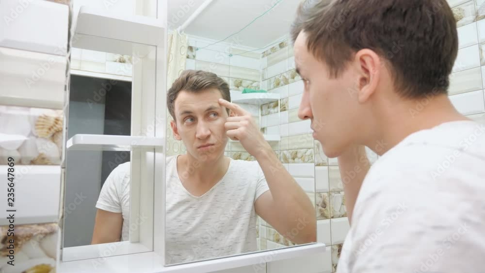 Young man checking his skin in bathroom. Young man checking his skin in bathroom.