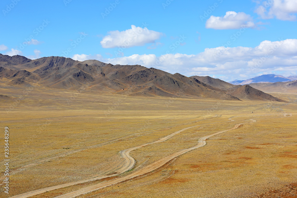 The rural road in the desert behind the mountain range with sky blue and cluods. Central Asia between the Russian Altai and Western Mongolia 