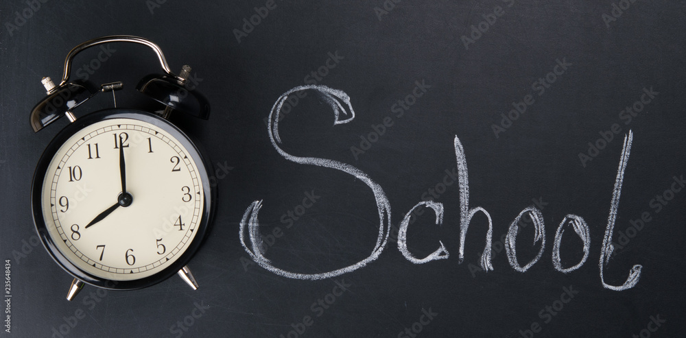 on the background of the black board written in chalk school, near the alarm clock on the background of the black board written in chalk school, near the alarm clock