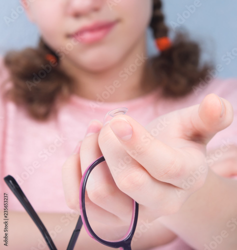 smile, close-up, hand holds eye glasses, and there is a lens on a finger to improve vision