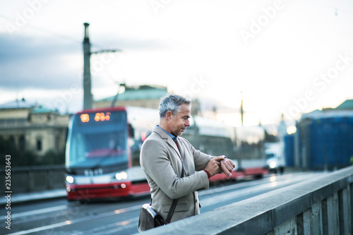 Photography Mature businessman standing on a bridge in Prague city, checking the time