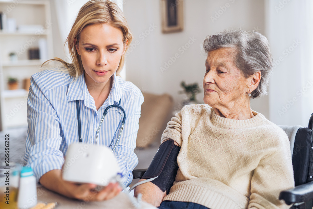 Obraz premium A health visitor measuring a blood pressure of a senior woman at home.