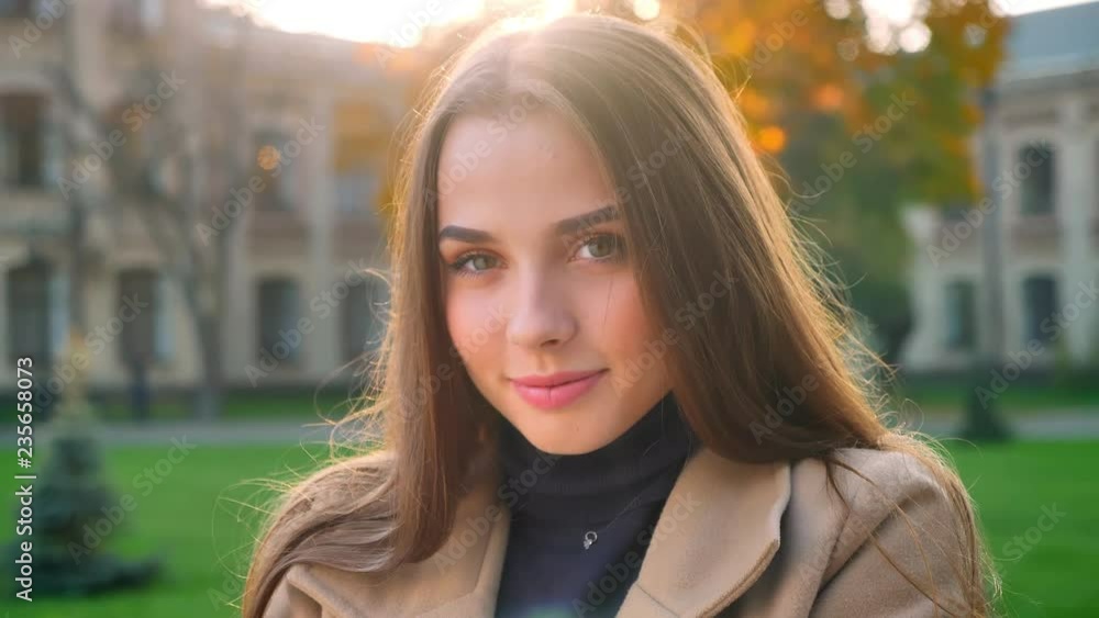 Pretty caucasian female is llooking startight at camera and smiling cheerfully while standing outdoor in sunshines a, sentient city on background , cute model is posing Pretty caucasian female is llooking startight at camera and smiling cheerfully while standing outdoor in sunshines a, sentient city on background , cute model is posing