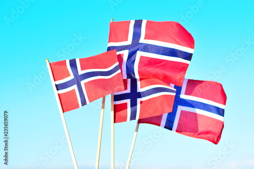 Four flags of Norway are fluttering in the wind against the blue sky and sea background. Concept of Norwegian Constitution Day.  Celebrated on May 17.