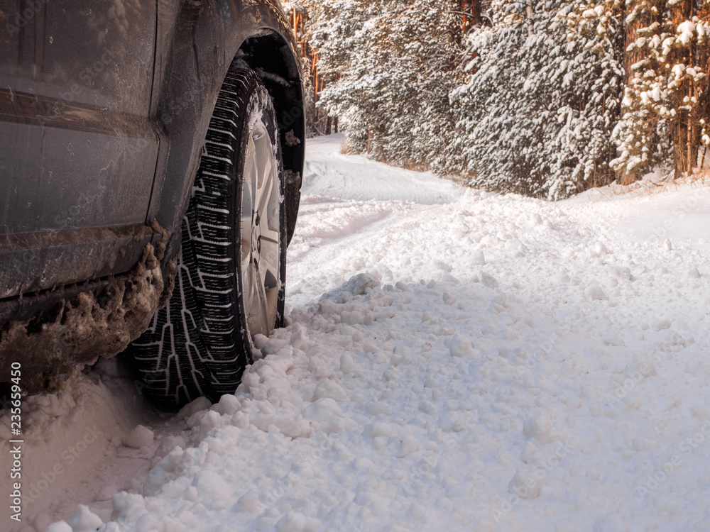 Luxury black crossover made a stop on the winter road in the forest. SUV. Car tires on winter road covered with snow. Vehicle on snowy alley in the morning at snowfall. Luxury black crossover made a stop on the winter road in the forest. SUV. Car tires on winter road covered with snow. Vehicle on snowy alley in the morning at snowfall.