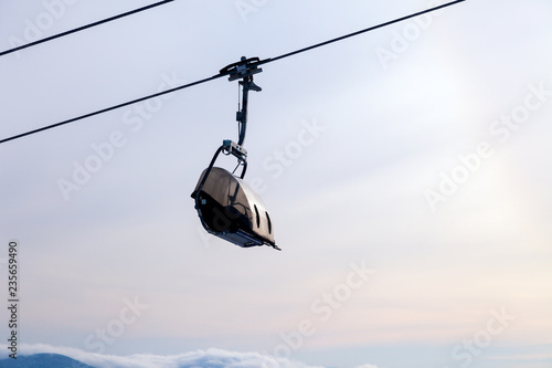 Closeup ski lift on the cable car with a closed cabin on the background of snow-capped mountain peaks, sun. Concept place for inscription, sunrise, sunshine, sunset