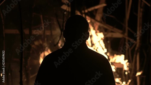 A man stands at a burning house, a man against a burning house at night