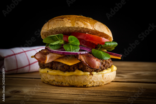 Regionaler und selbstgemachter Burger mit Geschirrtuch auf Holzbrett und schwarzen Hintergrund