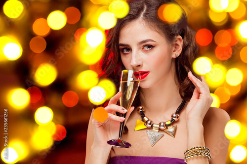 Beautiful girl holding a glass of champagne. Festive mood, shiny background with lights . Celebration of New Year and Christmas, white wine and excitement