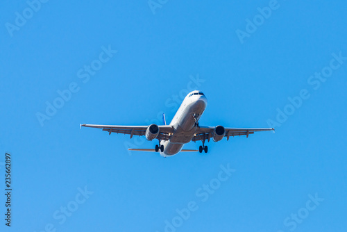 A white airplane flying in a clear pale blue sky