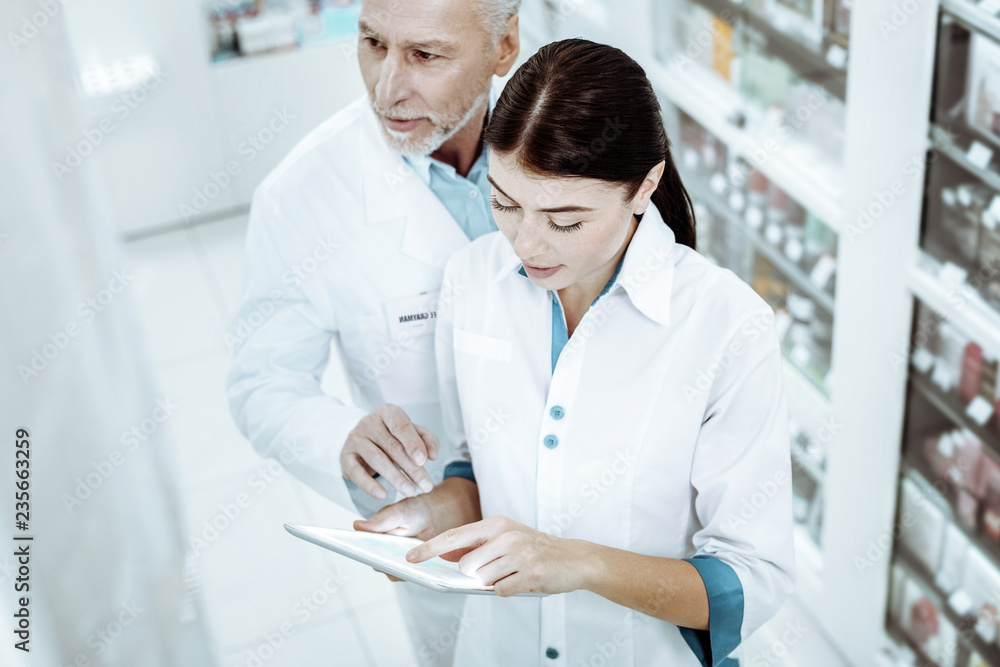 Competent pharmacist helping his assistant during work