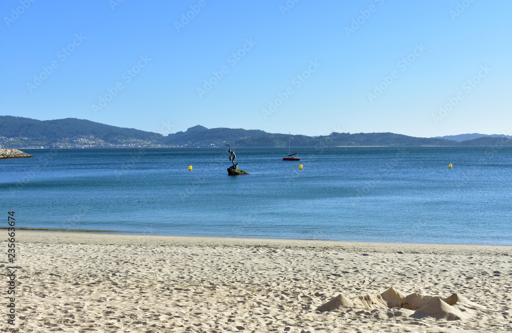 Beach with castle made of sand and statue. Golden sand, clear water, blue sky. Sanxenxo, Rias Baixas, Spain.