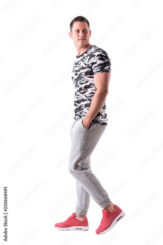 Happy macho sporty young man walking, smiling and looking back. Side view. Full body isolated on white background. Happy macho sporty young man walking, smiling and looking back. Side view. Full body isolated on white background.