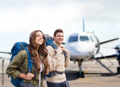 travel, tourism and people concept - couple of tourists with backpacks over plane on airfield background