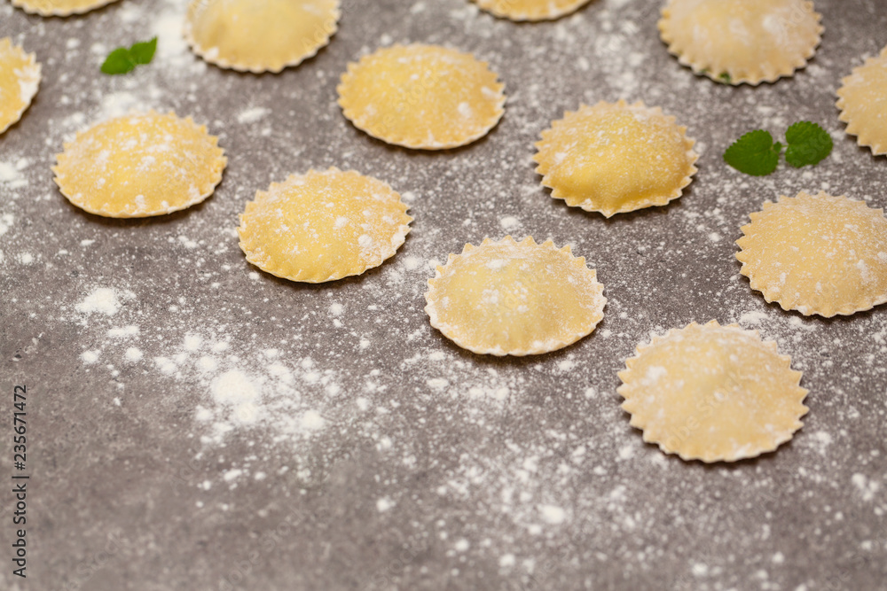 Tasty raw ravioli with flour on dark background. Process of making italian ravioli.