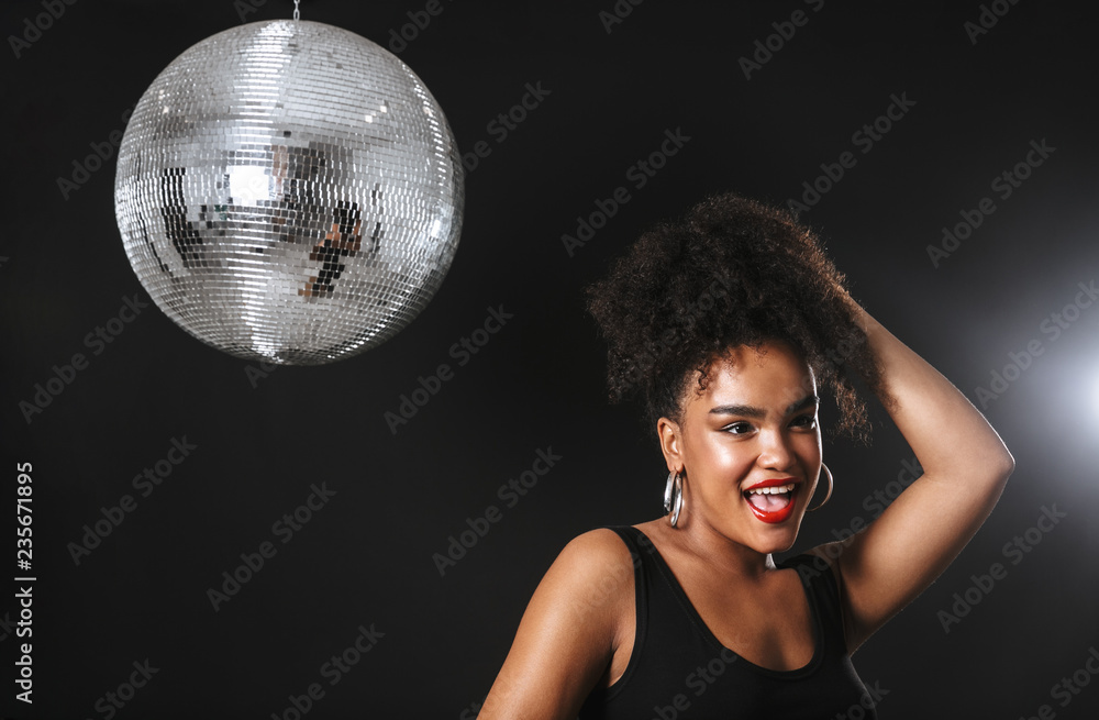 Naklejka premium Image of adorable african woman standing with silver disco ball, isolated over black background