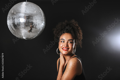 Image of beautiful african woman standing with silver disco ball, isolated over black background