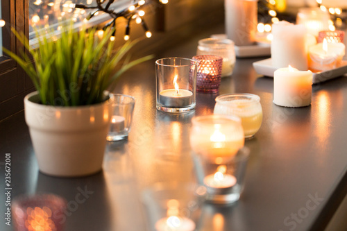 hygge  decoration and christmas concept - candles burning in lanterns and festive garland on window sill at home