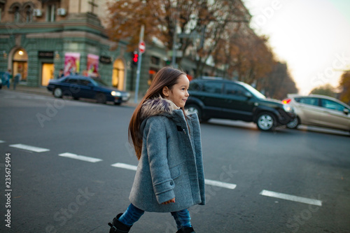 Child girl is walking across the city road at the crosswalk in evening.