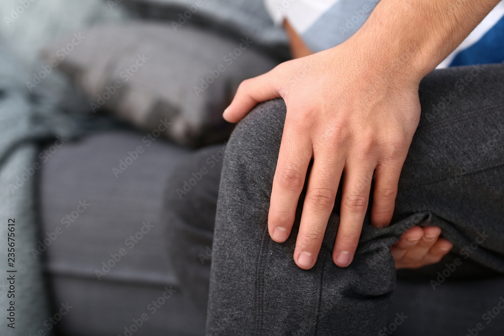 Young man suffering from pain in leg at home, closeup