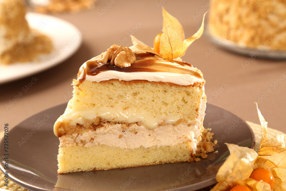 Macro close up of appetizing slice of white chocolate cake with nut and Physalis with out of focus cake in background. Macro close up of appetizing slice of white chocolate cake with nut and Physalis with out of focus cake in background.