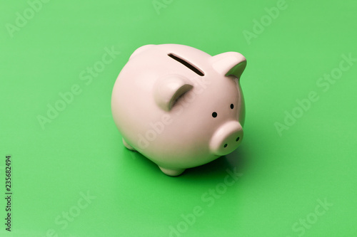 Pink piggy Bank in the shape of a pig stands in the center on a green background. Horizontal photography.