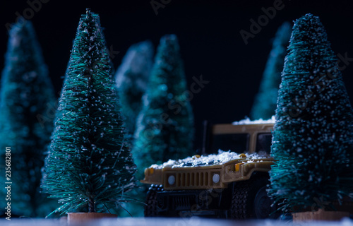 Toy military vehicle among toy christmas trees in winter