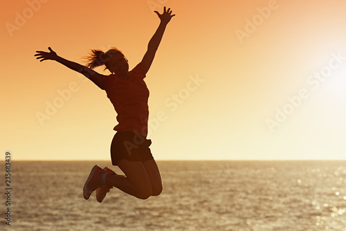 Silhouette of joyful woman jumping and having fun at the beach against the sunset, freedom and leisure vacation concept