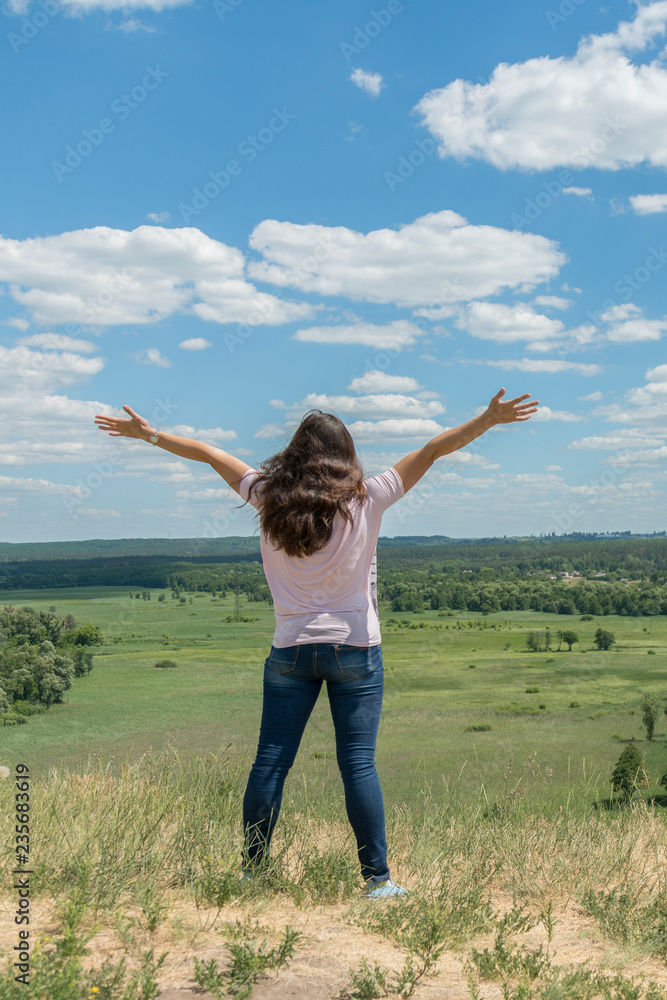 Young hipster girl is travelling in summer holidays. Woman in modern dress is standing on the hill and looking at the field. Blue sky and white clouds. Freedom and lifestyle concept. Beautiful nature. Young hipster girl is travelling in summer holidays. Woman in modern dress is standing on the hill and looking at the field. Blue sky and white clouds. Freedom and lifestyle concept. Beautiful nature.