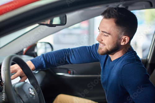 Brunette man with beard in blue sweater sitting in new car.