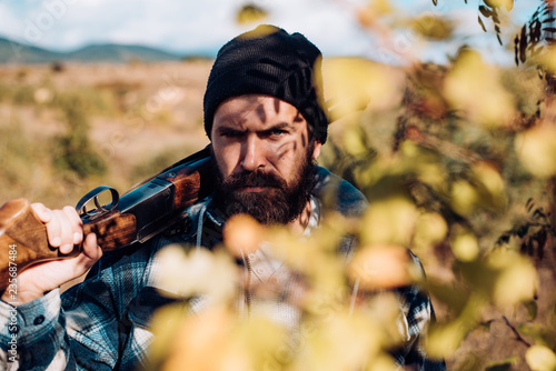 Bearded hunter man holding gun and walking in forest. Hunter with shotgun gun on hunt. Close up Portrait of hamdsome Hunter.