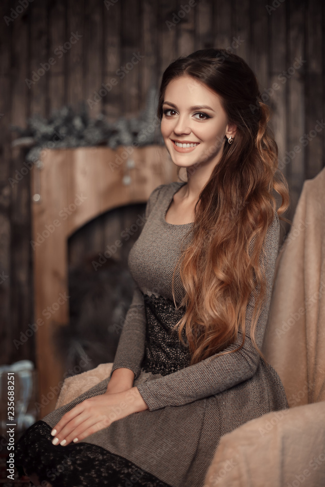 Close up portrait of young cheerful beautiful girl with dark long curly hair in gray dress in cozy interior. Brunette smiling with teeth, looking in camera with happy and relaxed face expression. Close up portrait of young cheerful beautiful girl with dark long curly hair in gray dress in cozy interior. Brunette smiling with teeth, looking in camera with happy and relaxed face expression.