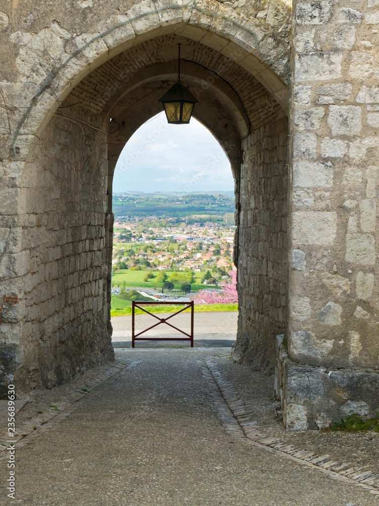 View over Villeneuve-sur-Lot through a gateway of the medieval hilltop village of Pujols, Lot-et-Garonne, France. Pujols is a member of Les Plus Beaux Villages de France association.