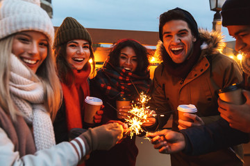 Young friends talking with each other drinking coffee outdoors winter concept holding bengal lights.