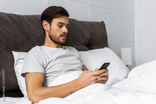 handsome bearded young man using smartphone in bed in the morning
