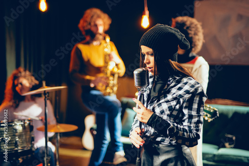 Band practice in home studio. Woman singing while rest of the band playing instruments. © chika_milan