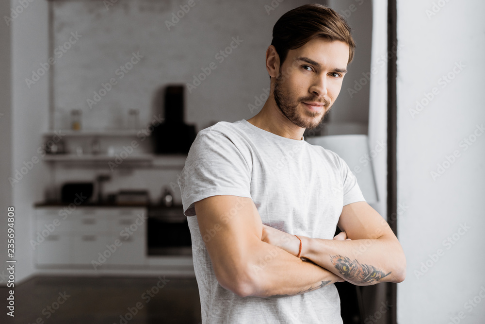 handsome young man with crossed arms looking at camera at home handsome young man with crossed arms looking at camera at home