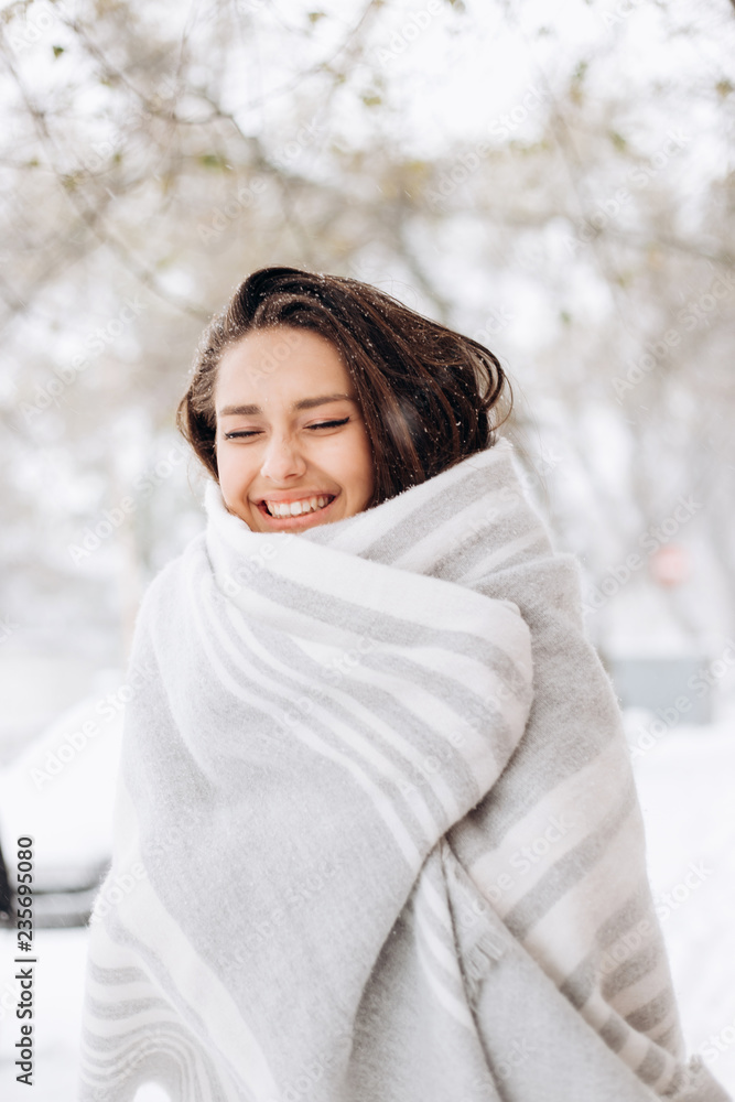 Smiling dark-haired girl wrapped in a gray scarf is standing in a snowy street on a winter day Smiling dark-haired girl wrapped in a gray scarf is standing in a snowy street on a winter day