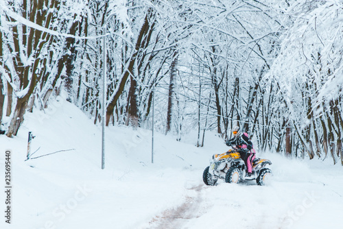 two persons ride quad bike in snowed forest