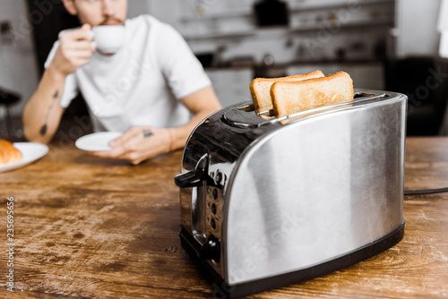 Fotografia cropped shot of young man drinking coffee at home with toaster on foreground