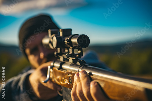 Close up snipers carbine at the outdoor hunting. Hunter aiming rifle in forest. Hunter with shotgun gun on hunt. Hunter with Powerful Rifle with Scope Spotting Animals.