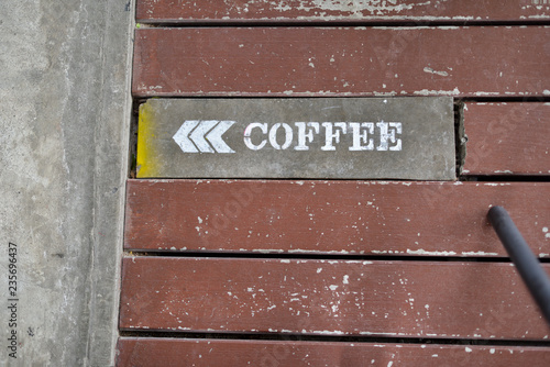 A white coffee sign with a white arrow indicated the entrance door on the wooden floor of the coffee shop.